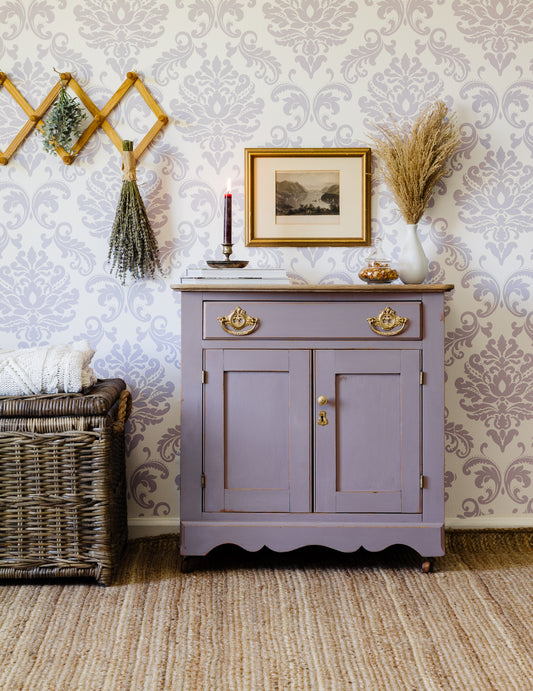 Lavande Homestead House Milk Paint cabinet against a patterned wallpaper wall with decorative elements.