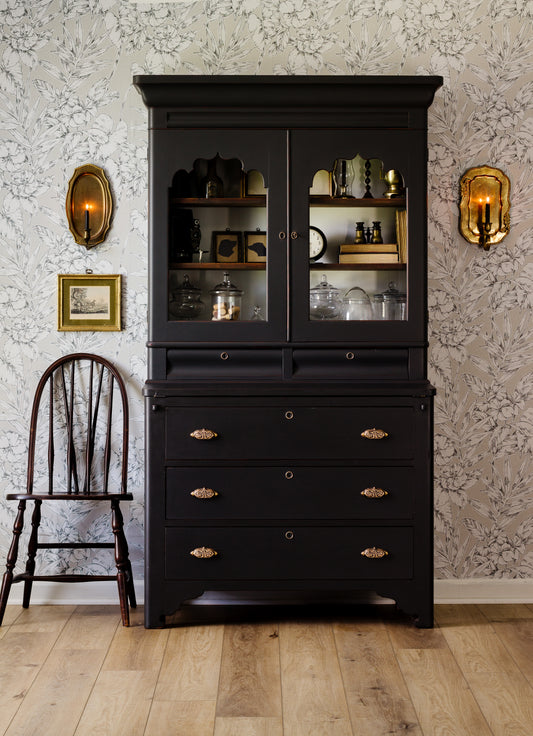 Coal Black smooth painted cabinet with glass doors against a patterned wall with two wall sconces.