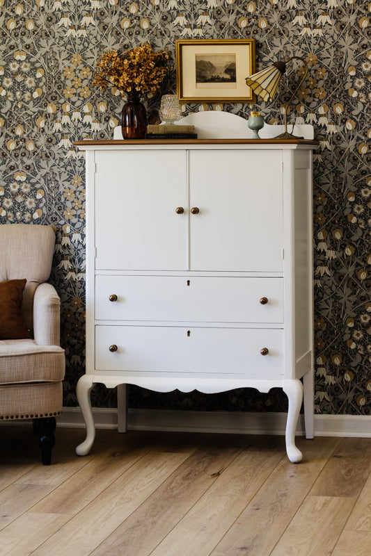 Porcelaine White homestead House milk paint dresser cabinet with decorative items against a dark william morris style patterned wall.