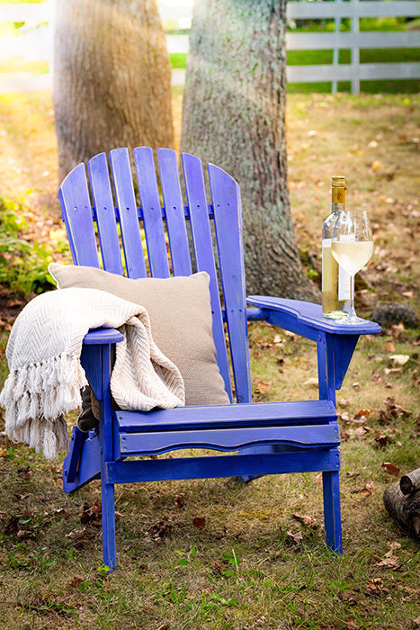 Blue Adirondack chair painted in St Laurent Homestead House Milk Paint with a pillow, blanket, and glass of wine on a grassy outdoor setting.