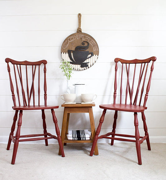 Two Barn Red wooden chairs in a room with a small wooden table and decorative wall art.