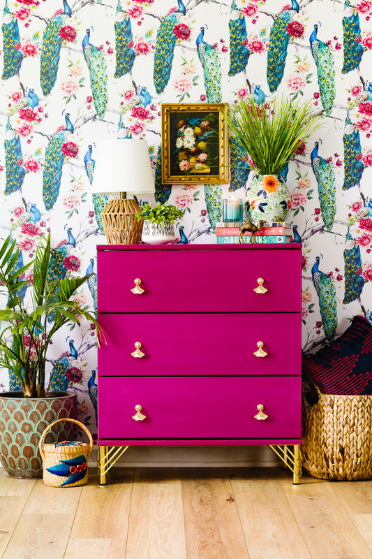 Fusia Pink dresser with gold legs and handles against a colorful floral wallpaper - Homestead House Milk Paint in Beret painted smoothly
