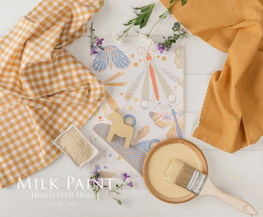 Swedish Yellow Milk paint inspiration board with a brush, fabric, and decorative elements on a white surface.