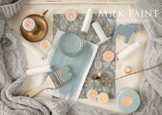 Milk paint inspiration board with paint brush and candles on a textured surface, featuring 'Homestead Home' brand.