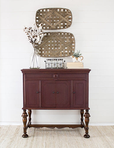 Smoothly painted Cranberry Homestead House Milk Paint Wooden sideboard with decorative baskets and books against a white wall.