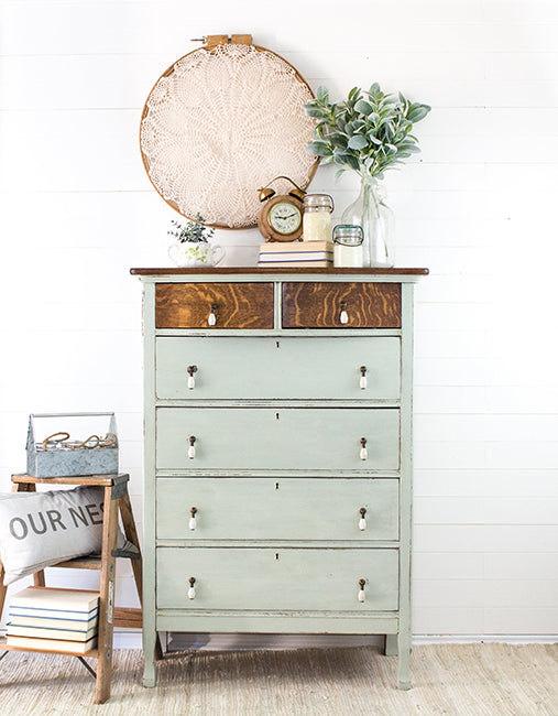 Two-toned dresser painted in pale green Craftsman Milk Paint with wooden feature drawer fronts and decorative items displayed on a white wall