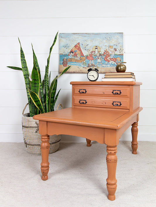 Wooden desk painted in autumn leaves homestead House Milk Paint with drawers, clock, and books against a white wall with a plant and artwork.