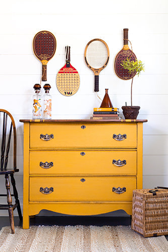 Bold Yellow dresser with vintage sports equipment and decor items against a white wall, painted in Homestead House Milk Paint Garden Seed