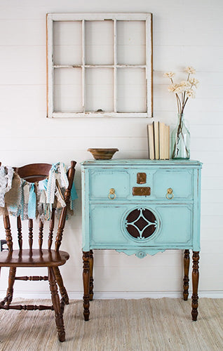 Vintage turquoise sideboard painted in Laurentian Homestead House Milk Paint with wooden chair and window frame against a white wall.