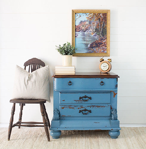 Maritime Blue Homestead House Milk Paint distressed chippy dresser with a wooden top, chair, and cpttage style decorative items against a white wall.
